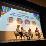 Quatre personnes sur une scène lors d'une conférence avec un grand écran derrière