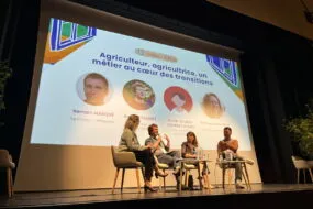 Quatre personnes sur une scène lors d'une conférence avec un grand écran derrière