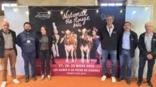 Des personnes posent devant une affiche du concours national bovin de race Pie Rouge