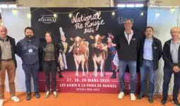 Des personnes posent devant une affiche du concours national bovin de race Pie Rouge