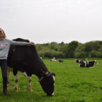 Une jeune femme souriante avec le bras sur une vache et le troupeau derrière