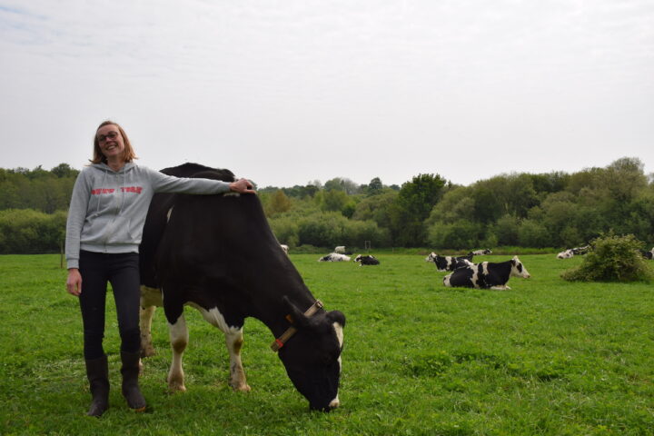 Une jeune femme souriante avec le bras sur une vache et le troupeau derrière