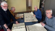 Quatre hommes feuillettent des journaux agricoles anciens