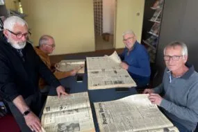 Quatre hommes feuillettent des journaux agricoles anciens