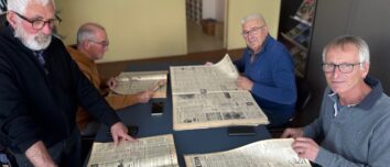Quatre hommes feuillettent des journaux agricoles anciens