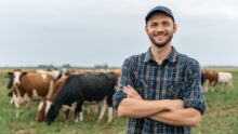 Un agriculteur souriant les bras croisés dans un champ avec des vaches