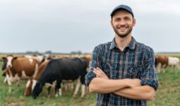 Un agriculteur souriant les bras croisés dans un champ avec des vaches