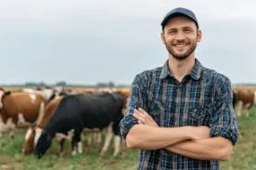 Un agriculteur souriant les bras croisés dans un champ avec des vaches