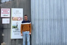 Un homme pose devant un bâtiment agricole