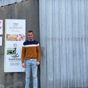 Un homme pose devant un bâtiment agricole