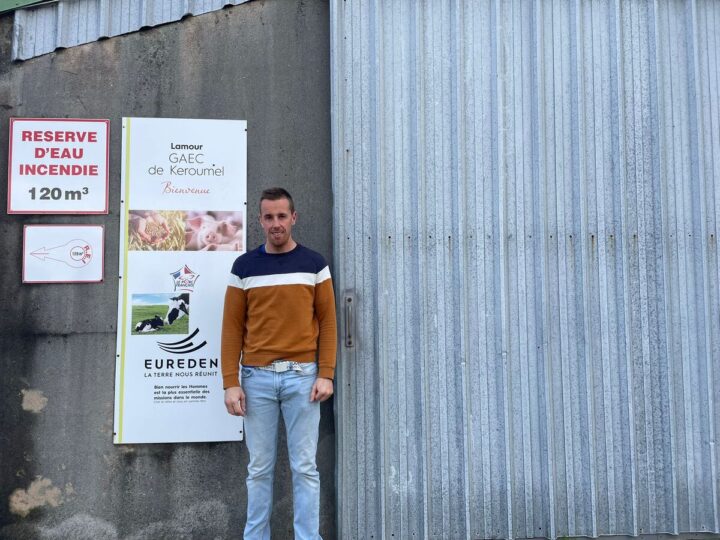 Un homme pose devant un bâtiment agricole
