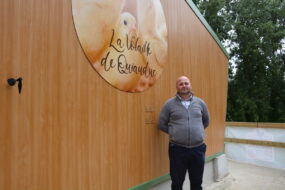 Un homme devant un bâtiment avec une enseigne d'élevage de volailles