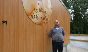 Un homme devant un bâtiment avec une enseigne d'élevage de volailles