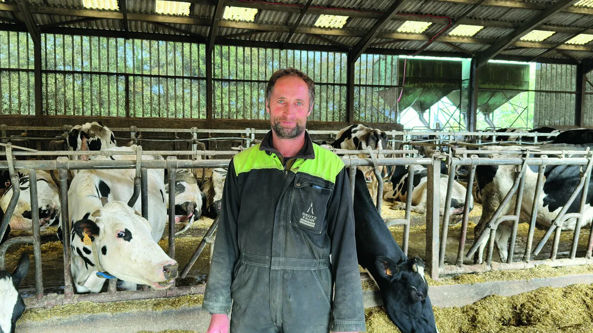 Un homme dans un bâtimentagricole avec des vaches au cornadis deriière - Illustration Quand la souplesse améliore le confort