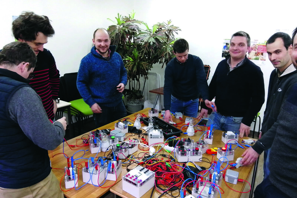 Des hommes autour d'une table avec du matérile d'électricité posé dessus - Illustration Reprendre les bases de l’électricité