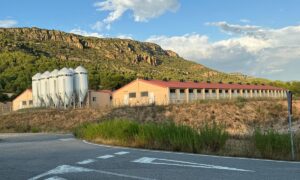 Un paysange de montagne ensoleillé avec un bâtiment d'élevage de porc et des silos à grain