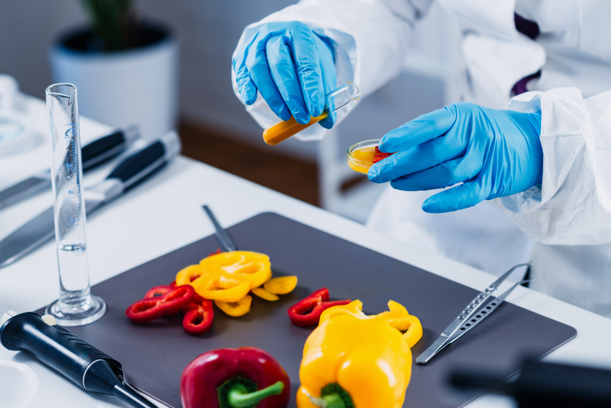 Gros plan sur les mains d'un scientifique qui porte des gants de laboratoire. Il analyse des poivrons - Illustration L’Europe mange ce qu’elle interdit