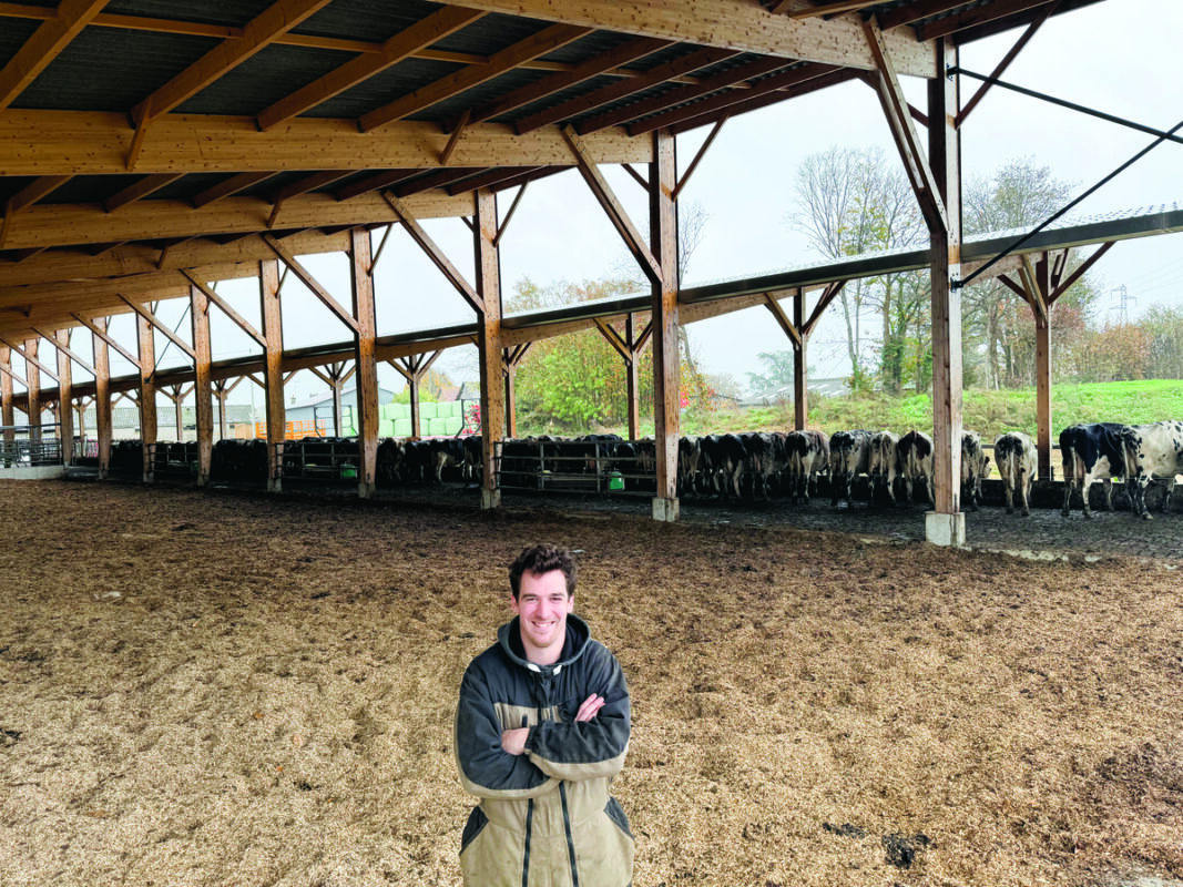 Un éleveur devant une litière pour vaches laitières dans une étable très ouverte