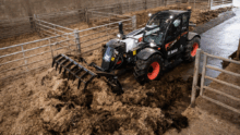 Un chariot télescopique équipé d'un godet à griffes en train de curer une stabulation