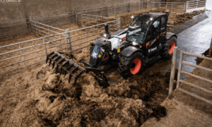 Un chariot télescopique équipé d'un godet à griffes en train de curer une stabulation