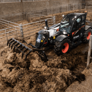 Un chariot télescopique équipé d'un godet à griffes en train de curer une stabulation