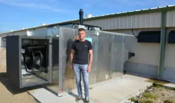 Un homme devant un système de chauffage d'un bâtiment d'élevage de volailles