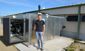 Un homme devant un système de chauffage d'un bâtiment d'élevage de volailles