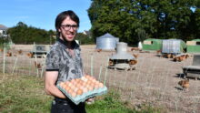 un éleveur qui tient des oeufs devant ses parcours de volaille