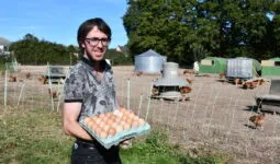 un éleveur qui tient des oeufs devant ses parcours de volaille
