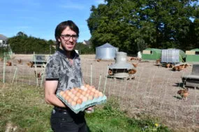 un éleveur qui tient des oeufs devant ses parcours de volaille