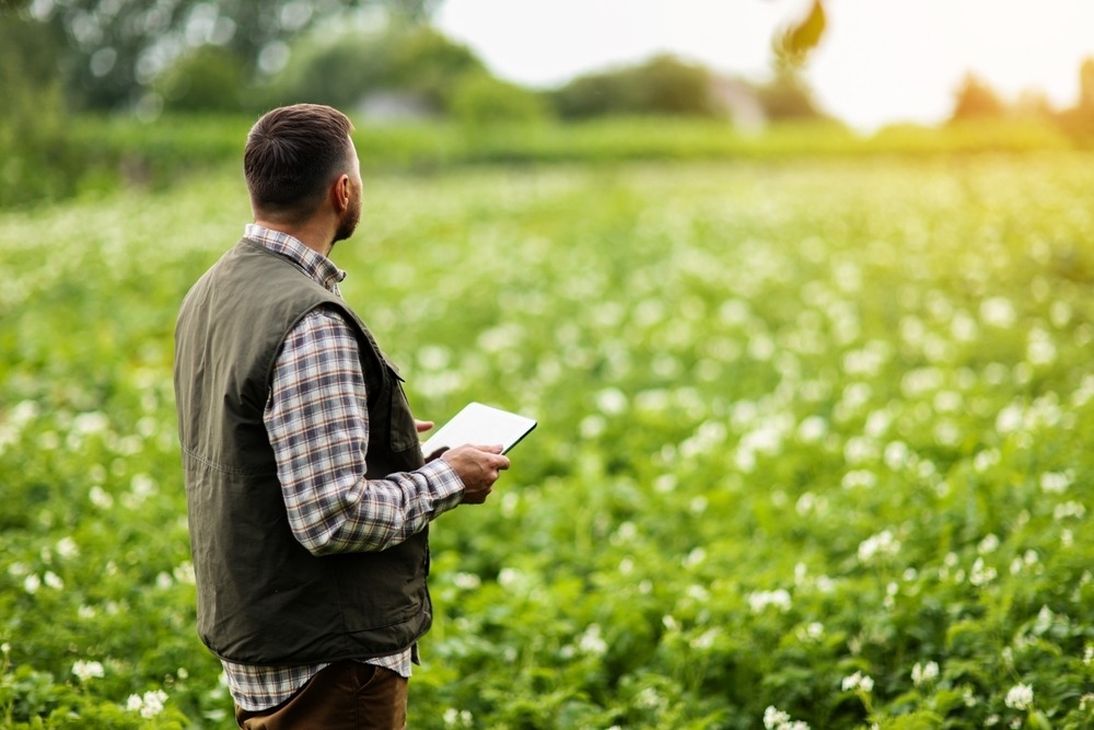 Un homme de dos avec une tablette à la main dans un champ - Illustration Votre projet agricole résilient mérite un « Coup de pousse » !