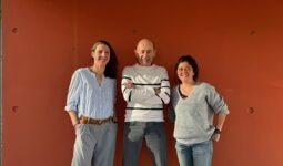 Deux femmes et un homme au centre devant un fond rouge