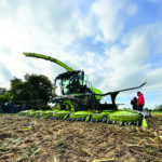 Une ensileuse au travail dans un champ de maïs avec des personnes sur le côté