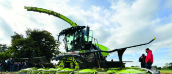 Une ensileuse au travail dans un champ de maïs avec des personnes sur le côté