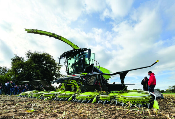Une ensileuse au travail dans un champ de maïs avec des personnes sur le côté