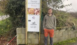 Un homme pose devant la pancarte de son élevage de porc