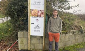 Un homme pose devant la pancarte de son élevage de porc
