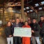 Des personnes dans une étable avec un imense chèque dans les mains