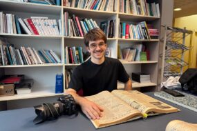 Un jeune photographe consulte un vieux journal d'archives devant des étagères remplies de livres.