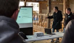 Des personnes dans un bâtiment d'élevage bovin avec en premier plan le dos d'un homme qui regarde un écran d'ordinateur