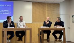 Qautre personnes à une tribune devant un grand écran