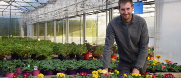Un homme dans une pépinière parmi ses étals de fleurs.