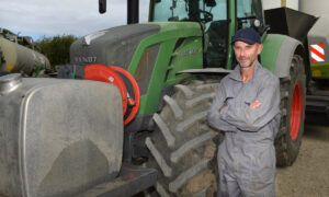 Un homme avec les bras croisés pose devant son tracteur