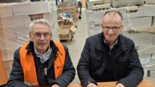 Deux hommes souriants assis à une table signent un contrat avec des palettes d'oeufs derrière