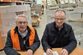 Deux hommes souriants assis à une table signent un contrat avec des palettes d'oeufs derrière
