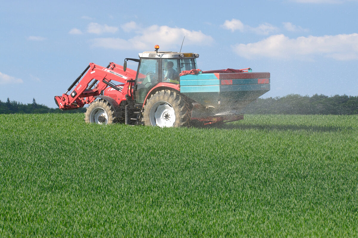 Un tracteur dans un champ avec un relevage à l'avant et un épandeur d'engrais à l'arrière - Illustration Des objectifs pour décarboner l&rsquo;agriculture