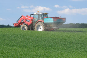 Un tracteur dans un champ avec un relevage à l'avant et un épandeur d'engrais à l'arrière