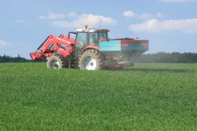 Un tracteur dans un champ avec un relevage à l'avant et un épandeur d'engrais à l'arrière