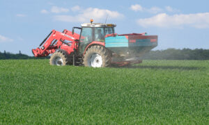 Un tracteur dans un champ avec un relevage à l'avant et un épandeur d'engrais à l'arrière