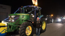 Un jeune agriculteur avec un bonnet de Noël devant un tracteur vert de marque John Deere